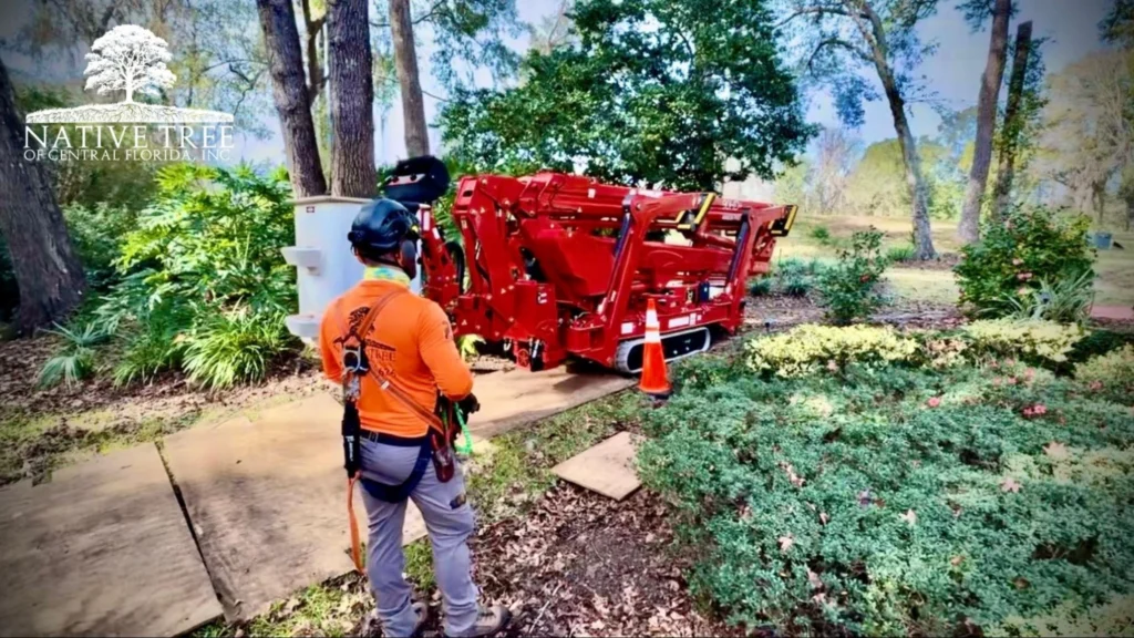 A man stands beside a red tree care machine, showcasing his expertise as a certified arborist in Ocala, Florida.